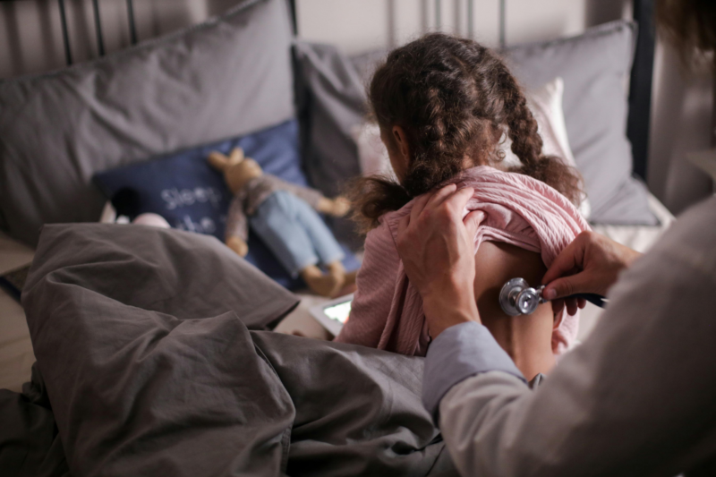 A child facing backward and a doctor using a stethoscope
