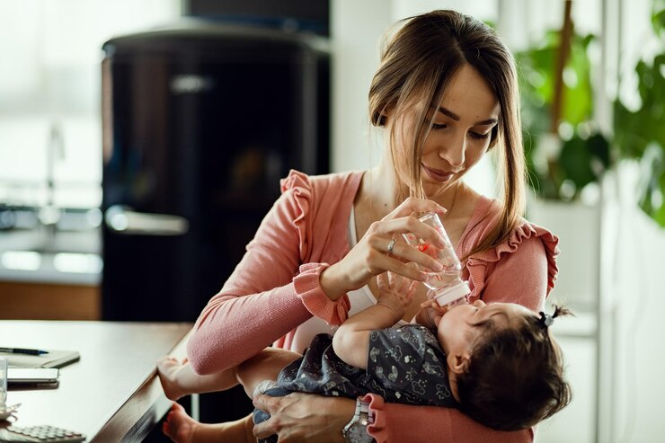 A mother sitting beside a table, bottle-feeding her baby.